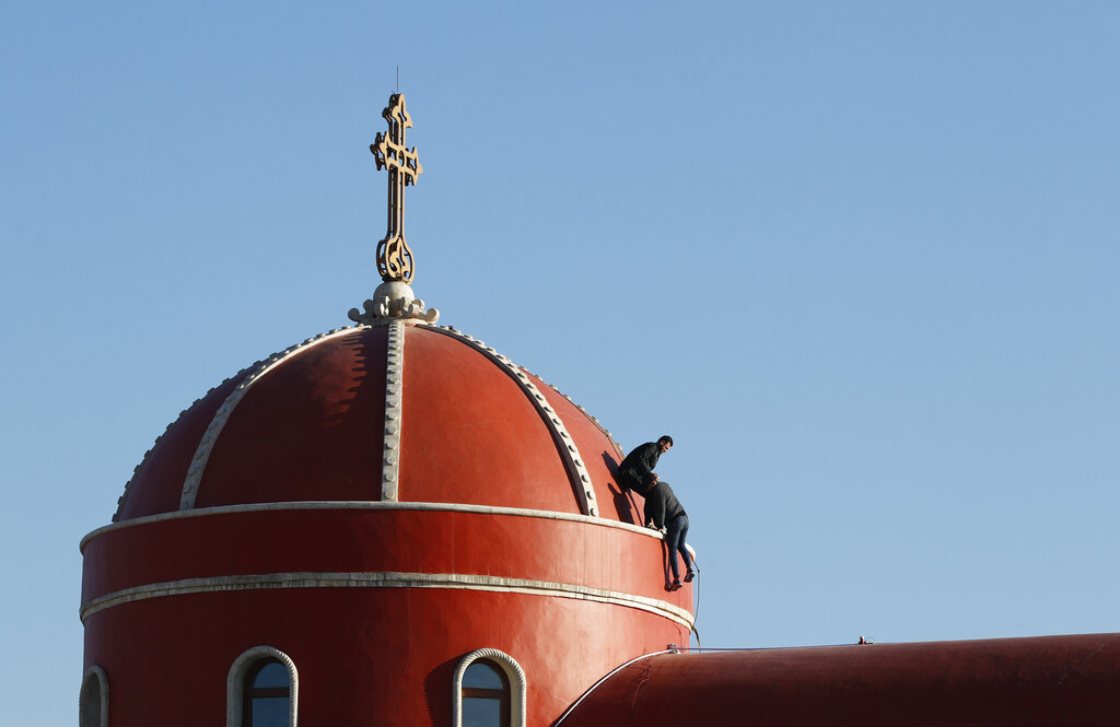 Iraqi Christians clean the the roof of the Church of the Immaculate Conception in Qaraqosh, Iraq, Tuesday, Feb. 23, 2021. Pope Francis will visit the church during his historic trip to Iraq.   Damaged during the Islamic State reign of terror, the church's tragedy mirrored that of its Christian community which was devastated by the group.  (AP Photo/Hadi Mizban)
