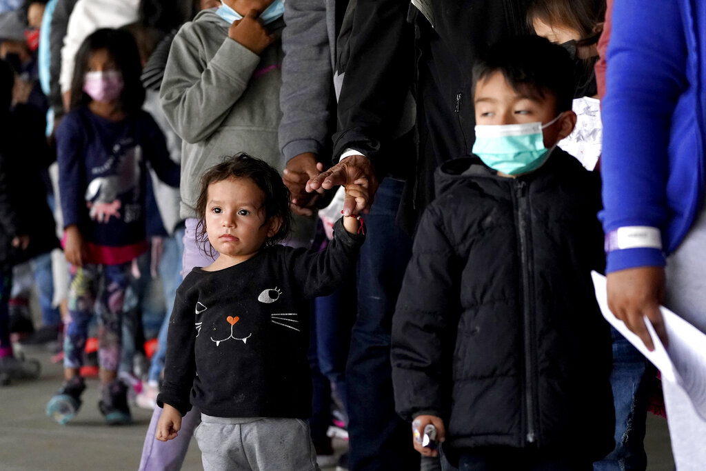 Migrant children are seen with adults as they wait in line to get a COVID-19 test before given travel instructions at a bus station, Wednesday, March 17, 2021, in Brownsville, Texas. A surge of migrants on the Southwest border has the Biden administration on the defensive. The head of Homeland Security acknowledged the severity of the problem Tuesday but insisted it's under control and said he won't revive a Trump-era practice of immediately expelling teens and children. An official says U.S. authorities encountered nearly double the number children traveling alone across the Mexican border in one day this week than on an average day last month. (AP Photo/Julio Cortez)