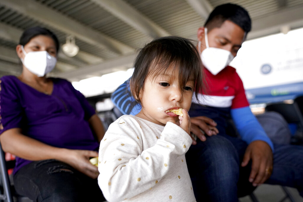 Larissa Bautista Hernandez, 2, a migrant from Honduras, eats a banana while waiting with her mother Irma Hernandez, left, and her father, Jose Frankis Bautista, for transportation at a bus station, Wednesday, March 17, 2021, in Brownsville, Texas. Bautista Hernandez's family is seeking asylum from the U.S. and is getting help from Team Brownsville, a humanitarian group, to reach their final destination with her uncle in South Carolina. A surge of migrants on the Southwest border has the Biden administration on the defensive. The head of Homeland Security acknowledged the severity of the problem Tuesday but insisted it's under control and said he won't revive a Trump-era practice of immediately expelling teens and children. (AP Photo/Julio Cortez)