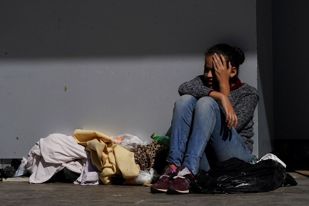 A migrant shields herself from the sun while resting at a plaza near the McAllen-Hidalgo International Bridge point of entry into the United States after being caught trying to sneak into the U.S. and deported, Thursday, March 18, 2021, in Reynosa, Mexico. A surge of migrants on the Southwest border has the Biden administration on the defensive. The head of Homeland Security acknowledged the severity of the problem Tuesday but insisted it's under control and said he won't revive a Trump-era practice of immediately expelling teens and children. (AP Photo/Julio Cortez)