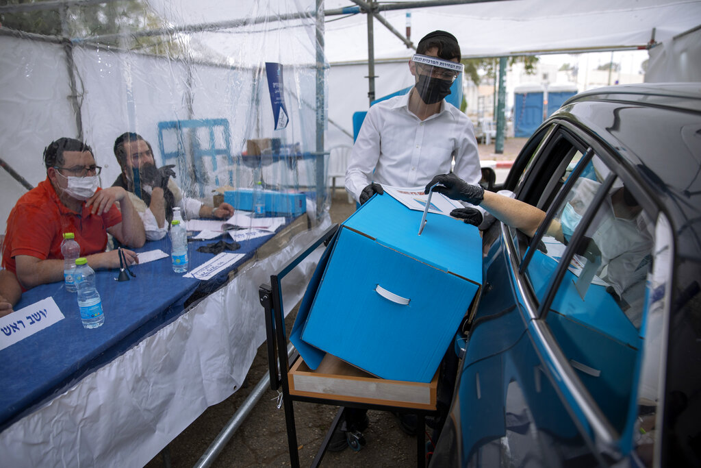 A women votes for Israel's parliamentary election at a special drive-in polling station for people who are in quarantine for coronavirus, in Ramat Gan, Israel, Tuesday, March. 23, 2021. Israel is holding its fourth election in less than two years.(AP Photo/Oded Balilty)