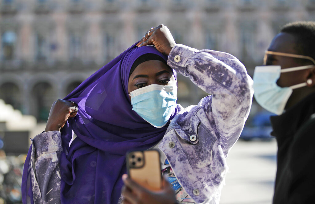 Influencer Moustapha Thiam holds up a phone for influencer Aida Diouf Mbengue as she adjusts her hijab in Piazza Duomo, in Milan, Italy, Tuesday, March 16, 2021. Mbengue, 19, from Senegal, is making a name for herself as a self-billed Afro-Influencer, one of a group of young people in Italy of African origin who have come together to try to increase their influence in social media. (AP Photo/Antonio Calanni)
