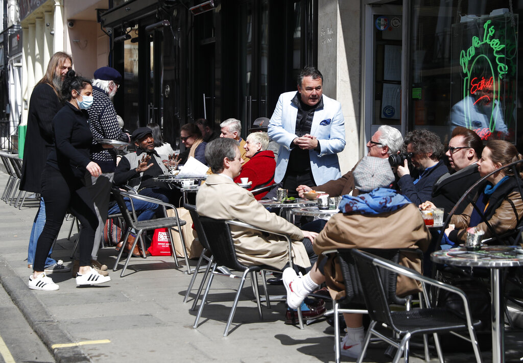 Patrons enjoy the sunshine as they sit outside eating and drinking in the Soho area of London, Monday, April 12, 2021, as restaurants, bars and pubs can open and serve people who can be seated outside. Millions of people in England will get their first chance in months for haircuts, casual shopping and restaurant meals on Monday, as the government takes the next step on its coronavirus lockdown-lifting road map. (AP Photo/Alastair Grant)