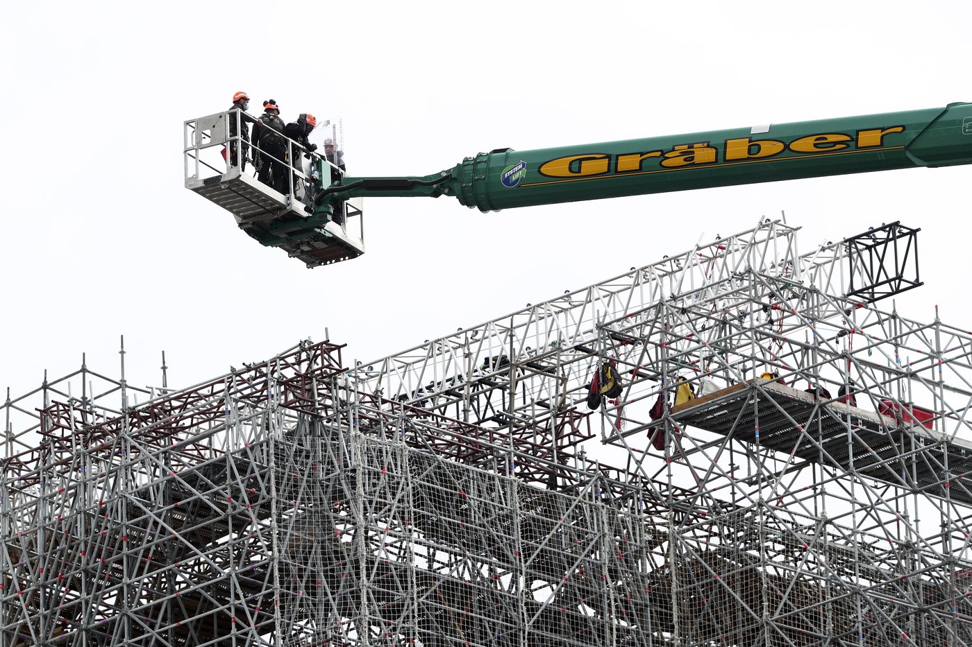 Workers are lifted onto the roof of Notre Dame cathedral, Monday, June 8, 2020 in Paris. Workers suspended from ropes will be lowered into the charred remains of scaffolding that melted atop Notre Dame when the cathedral went up in flames and begin the delicate job of dismantling the 200 tons of metal. (AP Photo/Thibault Camus)