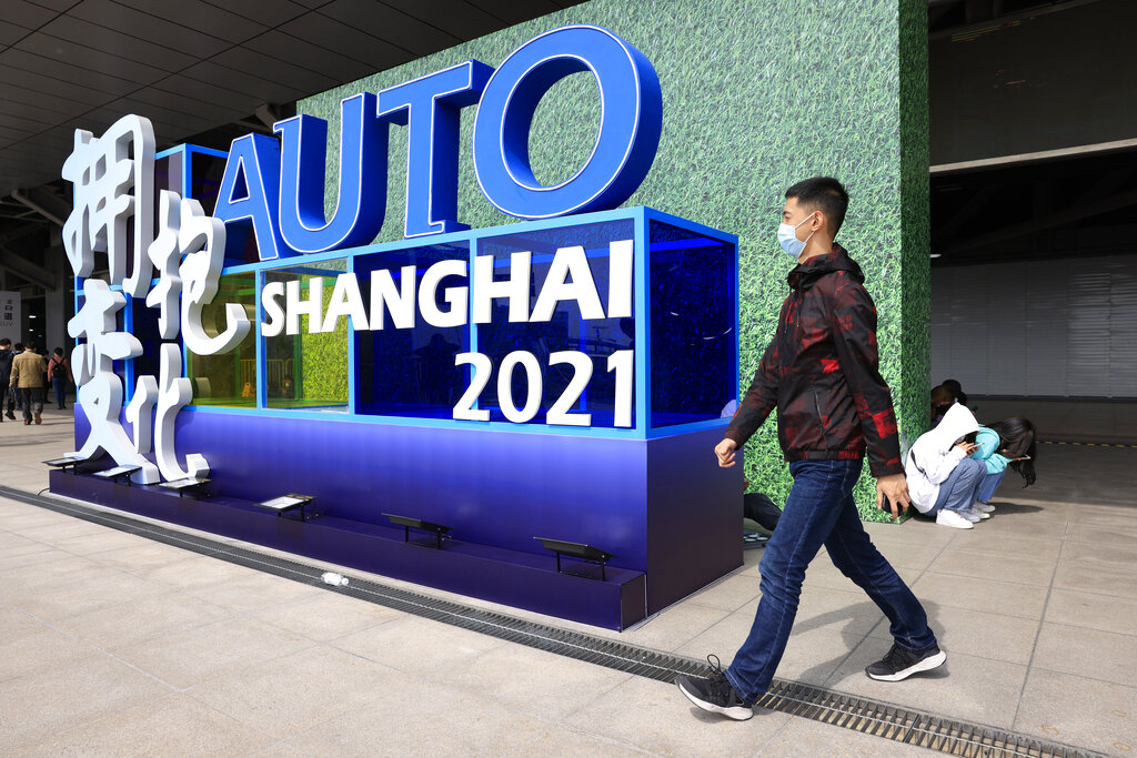 A man wearing a mask passes by a sign ahead of the Auto Shanghai 2021 show in Shanghai on Sunday, April 18, 2021. Automakers from around the world are showcasing their latest products this week in the world's biggest market for auto vehicles. (AP Photo/Ng Han Guan)