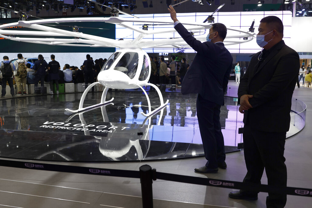 Workers stand near the volocopter flying vehicle displayed during the Shanghai Auto Show in Shanghai on Monday, April 19, 2021. Automakers are looking to China, their biggest market by sales volume and the first major economy to rebound from the pandemic, to revive sales and reverse multibillion-dollar losses. (AP Photo/Ng Han Guan)