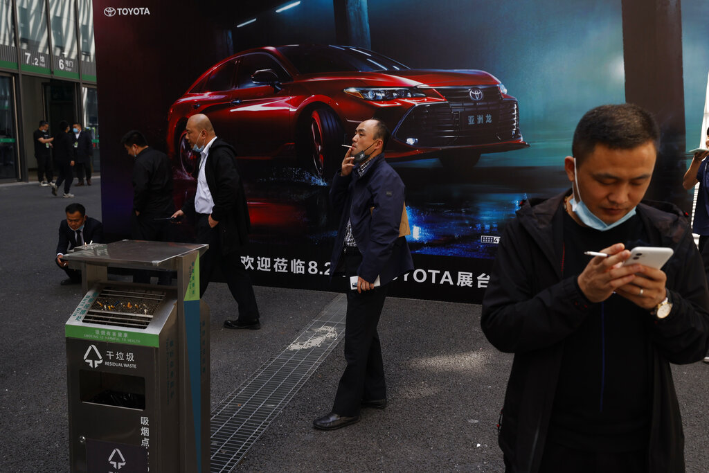 Chinese men smoke near a car advertisement during the Shanghai Auto Show in Shanghai on Monday, April 19, 2021. Automakers are looking to China, their biggest market by sales volume and the first major economy to rebound from the pandemic, to revive sales and reverse multibillion-dollar losses. (AP Photo/Ng Han Guan)