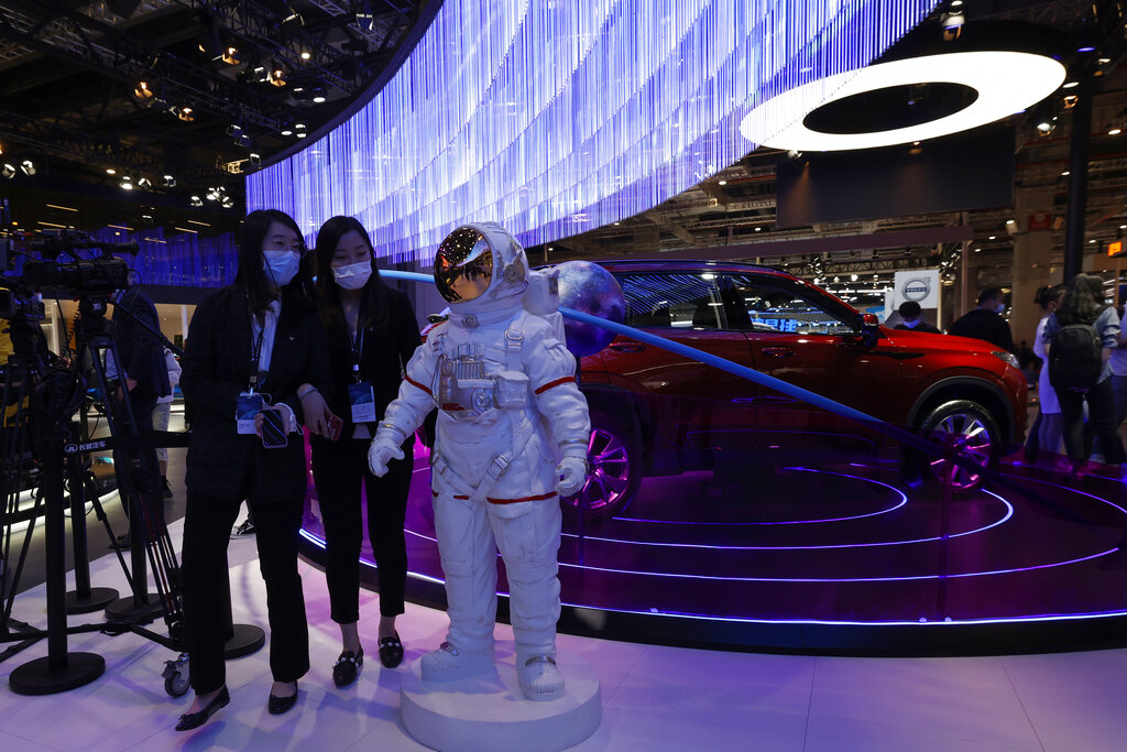 Visitors wearing mask walk by a figure of an astronaut displayed during the Shanghai Auto Show in Shanghai on Monday, April 19, 2021. Automakers are looking to China, their biggest market by sales volume and the first major economy to rebound from the pandemic, to revive sales and reverse multibillion-dollar losses. (AP Photo/Ng Han Guan)