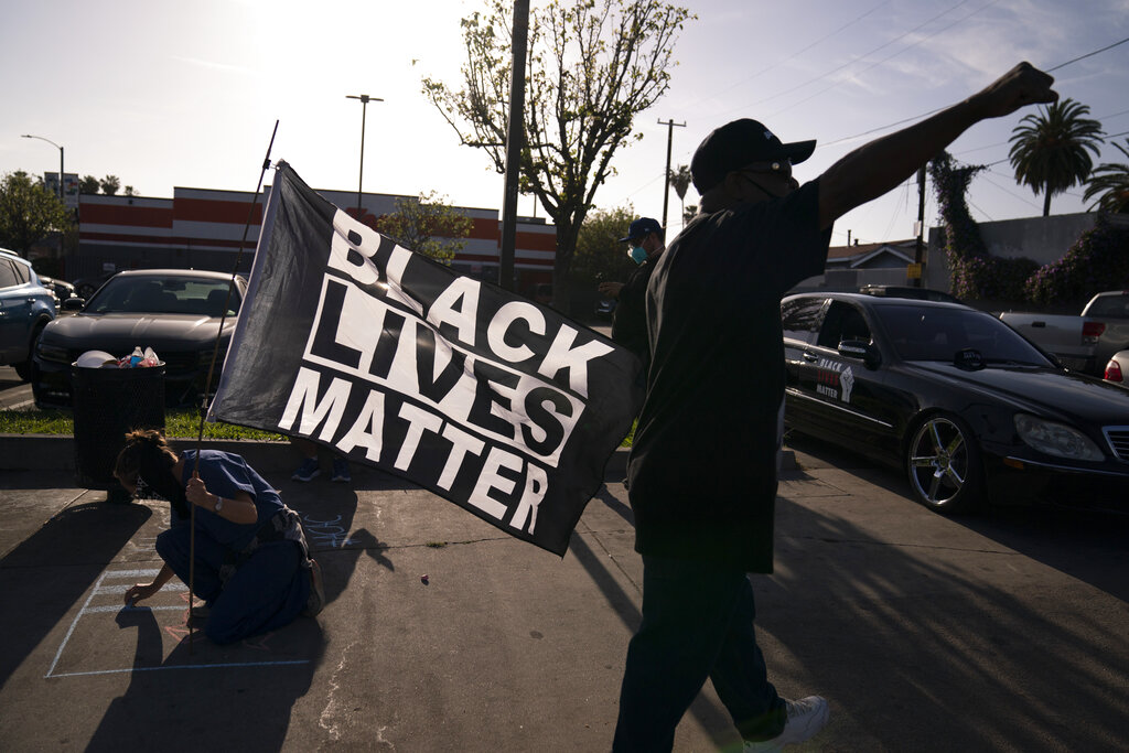 A woman with a Black Lives Matter flag writes a message on a sidewalk at the intersection of Florence and Normandie Avenues in Los Angeles, Tuesday, April 20, 2021, after a guilty verdict was announced at the trial of former Minneapolis police Officer Derek Chauvin for the 2020 death of George Floyd. (AP Photo/Jae C. Hong)