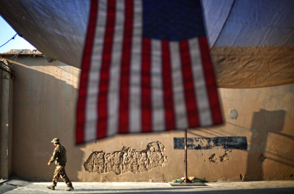 FILE - In this Sept. 11, 2011 file photo, a U.S. Army soldier walks past an American Flag hanging in preparation for a ceremony commemorating the tenth anniversary of the 9/11 attacks, at Forward Operating Base Bostick in Kunar province, Afghanistan. The final phase of ending America's “forever war” in Afghanistan after 20 years formally began Saturday, May 1, 2021, with the withdrawal of the last U.S. and NATO troops by the end of summer.(AP Photo/David Goldman, File)