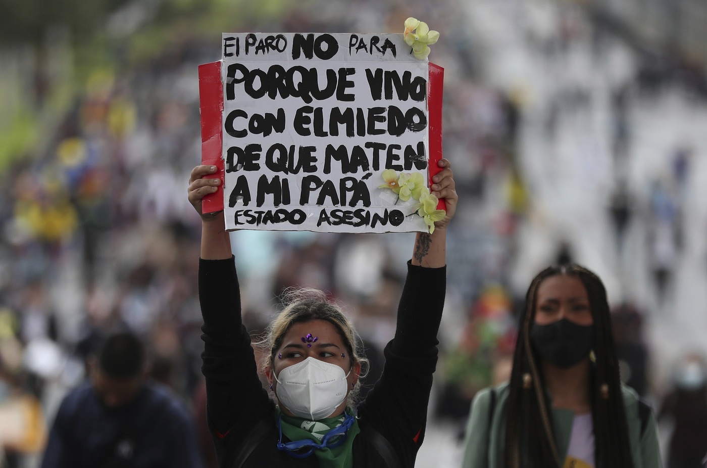 A woman holds a sign that reads in Spanish "Th strike does not stop, because I live in fear of my father being murdered," during a march by university students joining a national strike against tax reform, in Bogota, Colombia, Monday, May 3, 2021. Colombia's President Ivan Duque withdrew the government-proposed tax reform on Sunday. (AP Photo/Fernando Vergara)