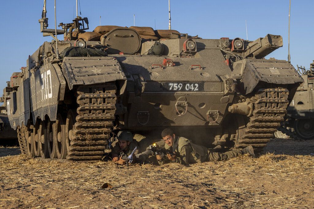 Israeli soldiers take cover under armored vehicles as a siren sounds warning of incoming rockets fired from Gaza strip in a staging ground near the Israeli-Gaza border southern Israel, Saturday, May 15, 2021. (AP Photo/Tsafrir Abayov)