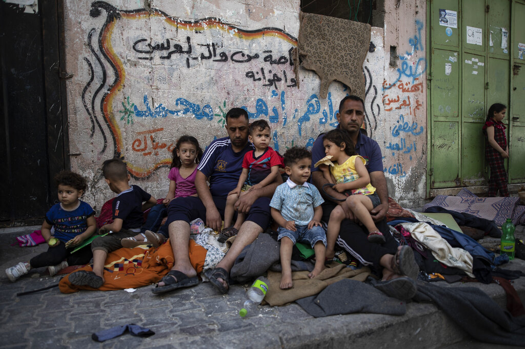 A Palestinian family sits outside their home after it was hit by an early morning Israeli airstrike, in Gaza City, Monday, May 17, 2021. (AP Photo/Khalil Hamra)
