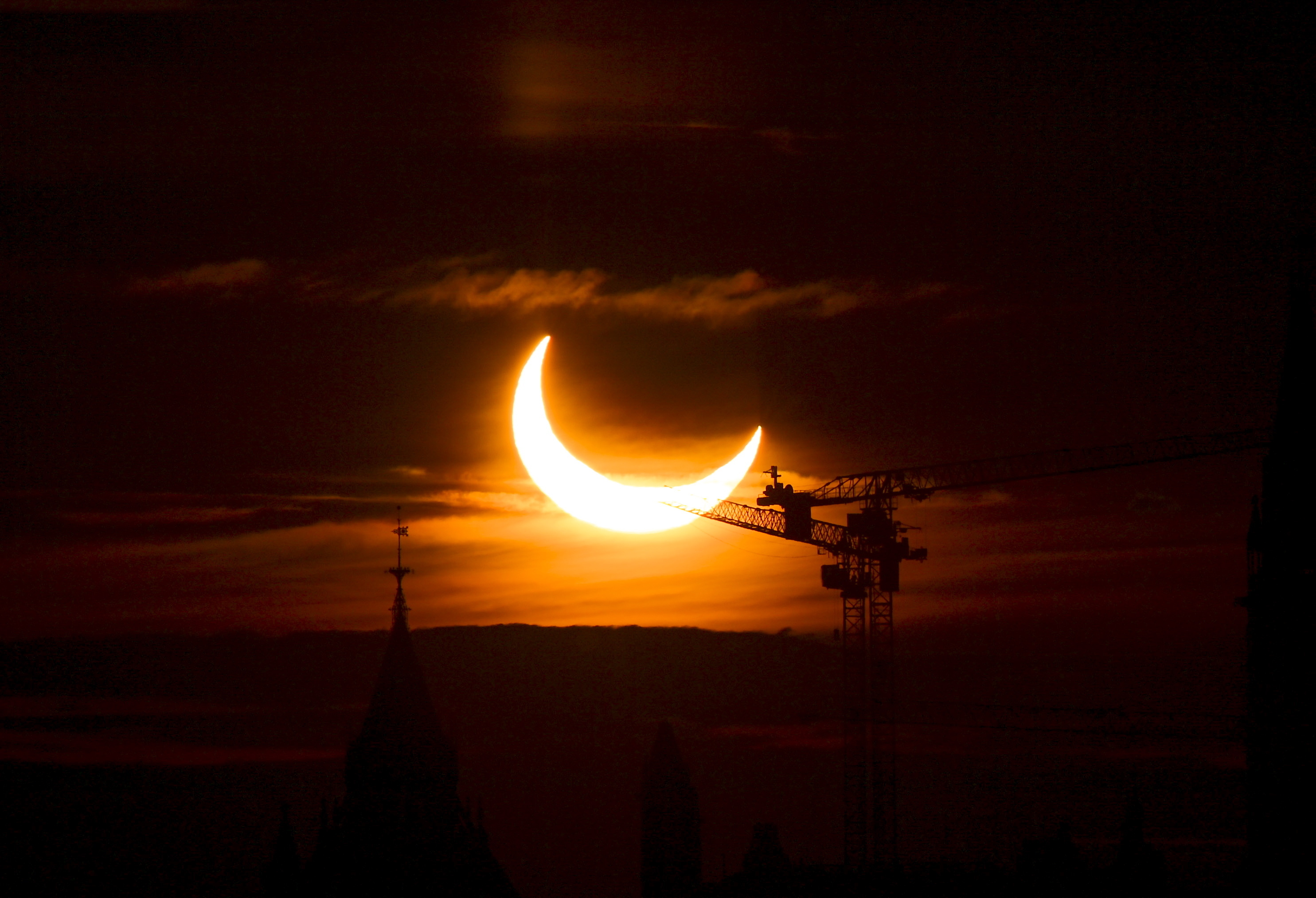 An annular solar eclipse rises over construction cranes and the Peace Tower on Parliament Hill in Ottawa on Thursday, June 10, 2021. (Sean Kilpatrick/The Canadian Press via AP)