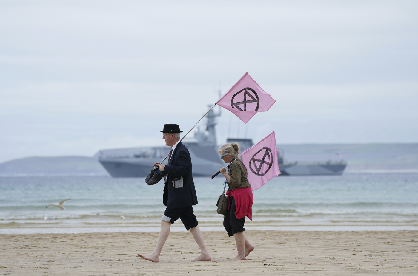 Two protestors holds flags as they walk on the beach of Carbis Bay during a demonstration outside the G7 meeting taking place in St. Ives, Cornwall, England, Friday, June 11, 2021. Leaders of the G7 begin their first of three days of meetings on Friday in Carbis Bay, in which they will discuss COVID-19, climate, foreign policy and the economy. (AP Photo/Jon Super)