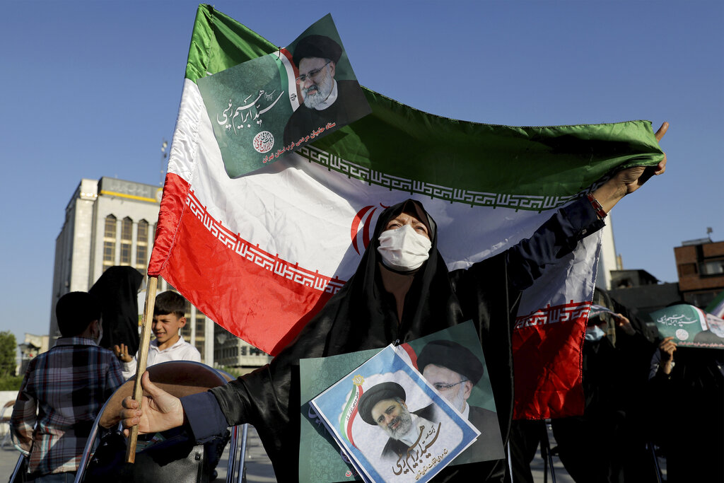 A supporter of presidential candidate Ebrahim Raisi holds signs and the Iranian flag during a rally in Tehran, Iran, Monday, June 14, 2021. Iran's clerical vetting committee has allowed just seven candidates for the Friday, June 18, ballot, nixing prominent reformists and key allies of President Hassan Rouhani. The presumed front-runner has become Ebrahim Raisi, the country's hard-line judiciary chief who is closely aligned with Supreme Leader Ayatollah Ali Khamenei. (AP Photo/Ebrahim Noroozi)