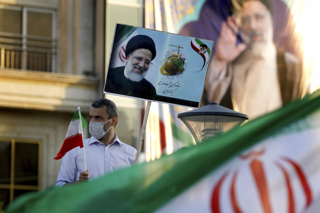 A supporter of presidential candidate Ebrahim Raisi hold signs and the Iranian flag during a rally in Tehran, Iran, Monday, June 14, 2021. Iran's clerical vetting committee has allowed just seven candidates for the Friday, June 18, ballot, nixing prominent reformists and key allies of President Hassan Rouhani. The presumed front-runner has become Ebrahim Raisi, the country's hard-line judiciary chief who is closely aligned with Supreme Leader Ayatollah Ali Khamenei. (AP Photo/Ebrahim Noroozi)