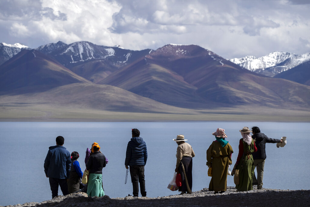 Tibetan Buddhist pilgrims stand on a bluff overlooking the lake in Namtso in western China's Tibet Autonomous Region, as seen during a government organized visit for foreign journalists, Wednesday, June 2, 2021. (AP Photo/Mark Schiefelbein)