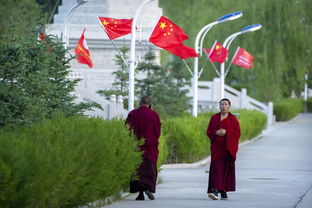 Monks walk along a sidewalk path lined with Chinese flags at the Tibetan Buddhist College near Lhasa in western China's Tibet Autonomous Region, Monday, May 31, 2021, as seen during a government organized visit for foreign journalists. High-pressure tactics employed by China's ruling Communist Party appear to be finding success in separating Tibetans from their traditional Buddhist culture and the influence of the Dalai Lama. (AP Photo/Mark Schiefelbein)