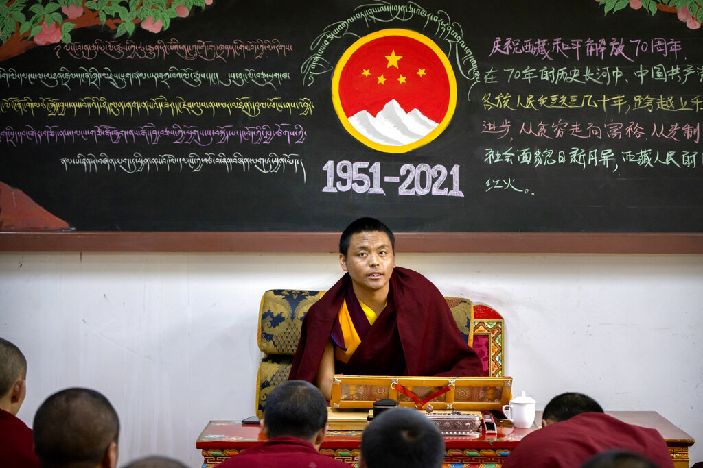 A monk teaches a class while sitting beneath a chalkboard with a mural commemorating the 70th anniversary of the Chinese government's control of Tibet at the Tibetan Buddhist College near Lhasa in western China's Tibet Autonomous Region, Monday, May 31, 2021, as seen during a government organized visit for foreign journalists. High-pressure tactics employed by China's ruling Communist Party appear to be finding success in separating Tibetans from their traditional Buddhist culture and the influence of the Dalai Lama. (AP Photo/Mark Schiefelbein)