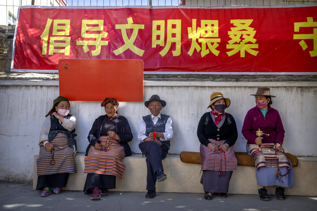 Members of the Buddhist faithful sit near a local holy site beneath a propaganda banner urging people to engage in a civilized manner in the Tibetan Buddhist practice of ritually burning pine branches in Lhasa in western China's Tibet Autonomous Region, Thursday, June 3, 2021, as seen during a government organized visit for foreign journalists. High-pressure tactics employed by China's ruling Communist Party appear to be finding success in separating Tibetans from their traditional Buddhist culture and the influence of the Dalai Lama. (AP Photo/Mark Schiefelbein)