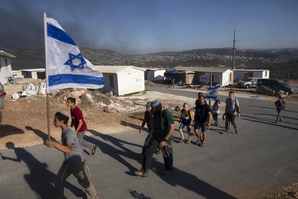 Israeli settlers carry an Israeli flag at the outpost of Eviatar near the northern West Bank town of Nablus, Monday, June 21, 2021. Settlers established the outpost last month and say it is now home to dozens of families. Palestinians say it is built on private land and fear it will grow and merge with other large settlements nearby. (AP Photo/Sebastian Scheiner)