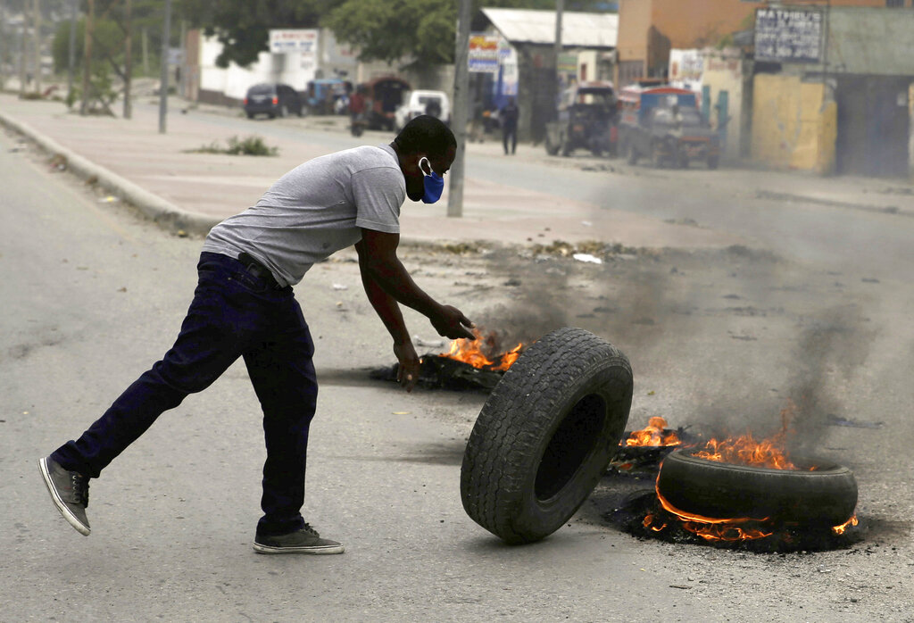 A supporter of former Senator Youri Latortue and Steven Benoit sets fire to tires outside of Haiti's courthouse in Port-au-Prince, Monday, July 12, 2021. Prosecutors have requested that high-profile politicians like Latortue and Benoit meet officials for questioning as part of the investigation into the assassination of President Jovenel Moise. (AP Photo/Joseph Odelyn)