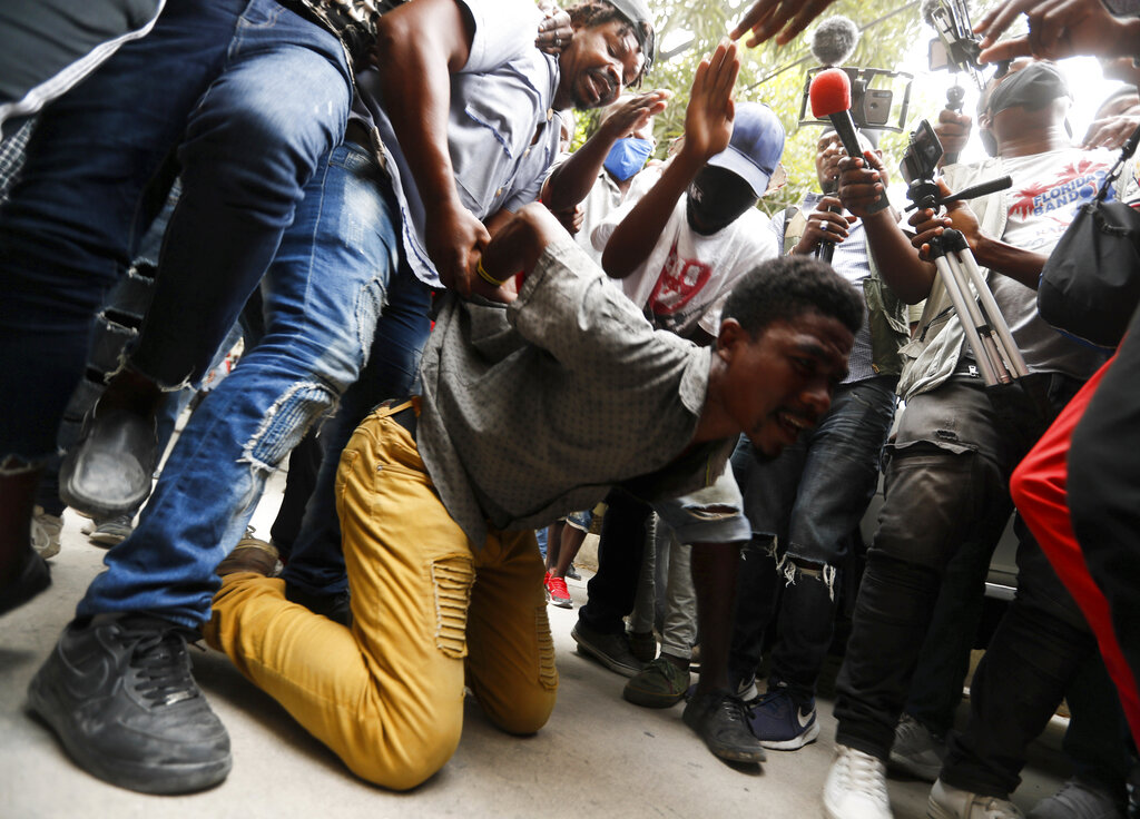 Supporters of former Senator Steven Benoit perform a mock execution for the adversaries of the senator, outside the courthouse as he departs after being called in for questioning in Port-au-Prince, Monday, July 12, 2021. Prosecutors have requested that high-profile politicians like Benoit meet officials for questioning as part of the investigation into the assassination of President Jovenel Moise. (AP Photo/Fernando Llano)