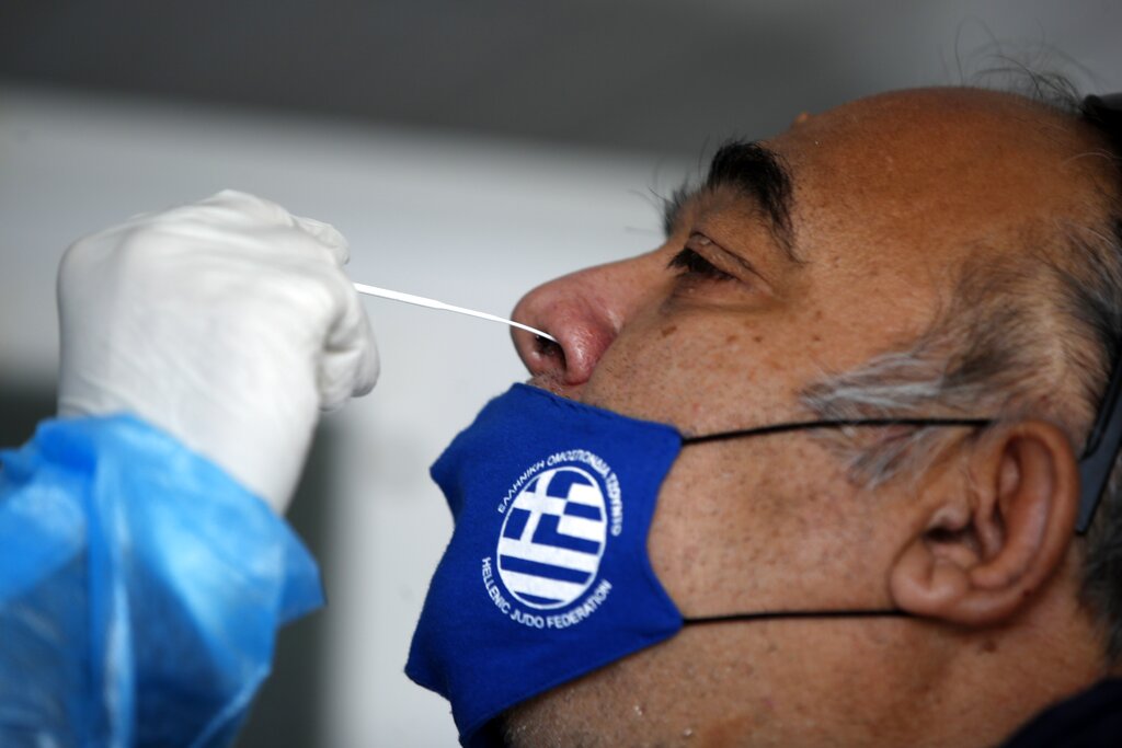 A medical staff member from the National Health Organization (EODY) conducts a rapid COVID test on a man, wearing a face mask with the Greek flag, in Athens, Thursday, Nov. 5, 2020. Greek Prime Minister Kyriakos Mitsotakis has announced a nationwide three-week lockdown starting Saturday morning, saying that the increase in the coronavirus infections must be stopped before Greece's health care system comes under 