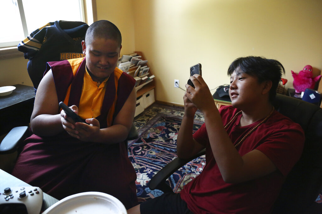 Jalue Dorje, left, and his cousin Delek Topgyal, 13, watch videos on their phones after playing the NBA 2K video game between prayer sessions on Monday, July 19, 2021, in Columbia Heights, Minn. (AP Photo/Jessie Wardarski)