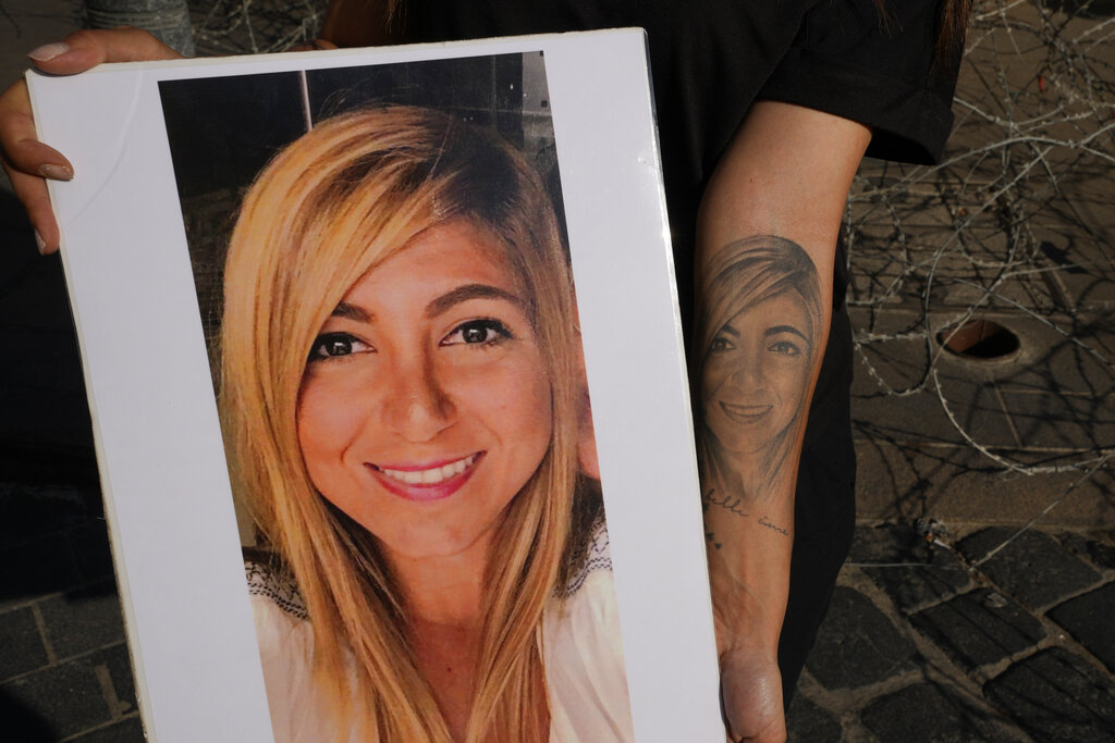 Mariana Fodoulian shows a tattoo and a portrait of her late sister Gaya Fodoulian during a protest near the parliament building to demand an expedited investigation, in Beirut, Lebanon, Sunday, July 4, 2021. Gaya Fodoulian died during the Aug. 4, 2020, Beirut port explosion. A year after the blast, families of the victims are consumed with winning justice for their loved ones and punishing Lebanon's political elite, blamed for causing the disaster through their corruption and neglect. Critics say the political leadership has succeeded so far in stonewalling the judicial investigation into the explosion. (AP Photo/Hassan Ammar)