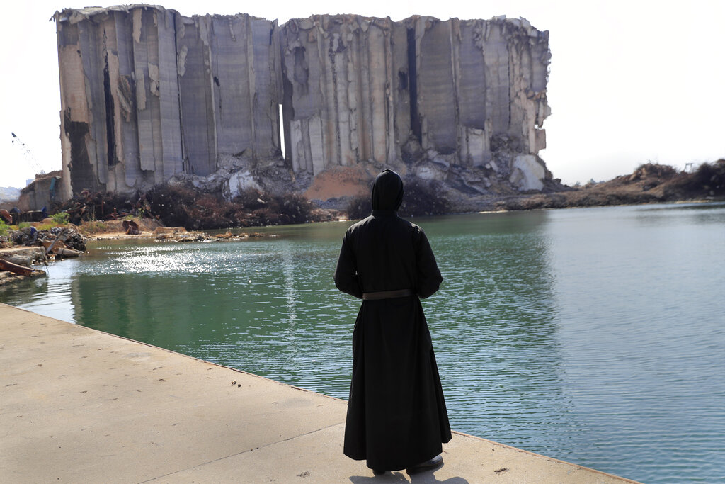 A priest looks towards the towering grain silos, that were gutted in the massive explosion last August, where a Mass will be held to commemorate the first year anniversary of the deadly blast, in Beirut seaport, Lebanon, Wednesday, Aug. 4, 2021. The grim anniversary comes amid an unprecedented economic and financial meltdown and a political stalemate that has kept the country without a functioning government for a full year. (AP Photo/Hussein Malla)