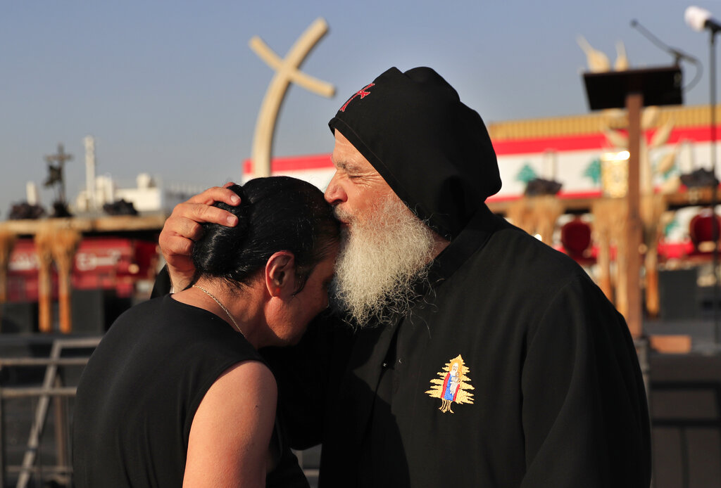 A priest kisses and comforts a relative of a victim who was killed in the massive blast last year at the Beirut port at a Mass held to commemorate the first year anniversary of the deadly blast, at the Beirut port, Lebanon, Wednesday, Aug. 4, 2021. United in grief and anger, families of the victims and other Lebanese came out into the streets of Beirut on Wednesday to demand accountability as banks, businesses and government offices shuttered to mark one year since the horrific explosion. (AP Photo/Hussein Malla)