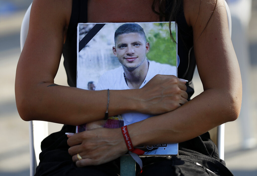 A relative of a victim who was killed in the massive blast last year at the Beirut port holds hugs his portrait as she attends a mass held to commemorate the first year anniversary of the deadly blast, at the Beirut port, Lebanon, Wednesday, Aug. 4, 2021. United in grief and anger, families of the victims and other Lebanese came out into the streets of Beirut on Wednesday to demand accountability as banks, businesses and government offices shuttered to mark one year since the horrific explosion. (AP Photo/Hussein Malla)