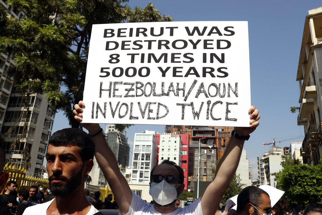 An anti-government protester holds a placard during a protest marking the first anniversary of the massive blast at Beirut's port, near Parliament Square, in Beirut, Lebanon, Wednesday, Aug. 4, 2021.  The grim anniversary comes amid an unprecedented economic and financial meltdown and a political stalemate that has kept the country without a functioning government for a full year. (AP Photo/Bilal Hussein)