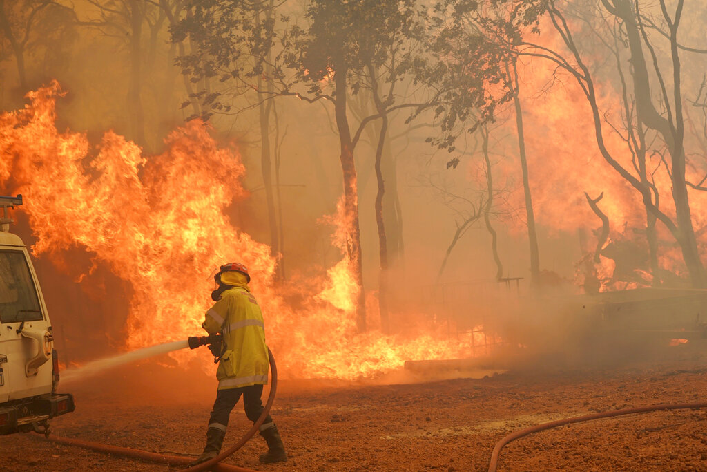 In this photo provided by Department of Fire and Emergency Services, a firefighter attends to a fire near Wooroloo, northeast of Perth, Australia, Tuesday, Feb. 2, 2021. An out-of-control wildfire burning northeast of the Australian west coast city of Perth has destroyed dozens of homes and was threatening more. (Evan Collis/DFES via AP)