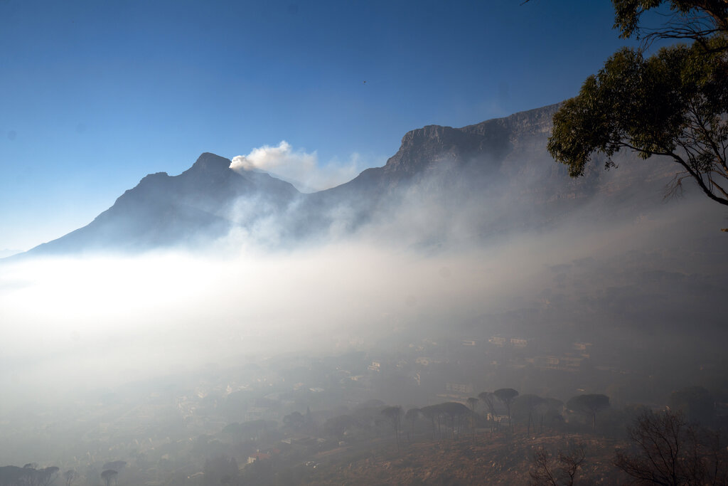 Smoke engulfs the city of Cape Town, South Africa, Tuesday April 20, 2021. A massive fire spreading on the slopes of the city's famed Table Mountain, at right, is kept under control as firemen and helicopters take advantage of the low winds to contain the blaze. (AP Photo/Jerome Delay)