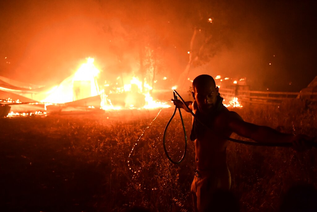 A man uses a water hose during a wildfire in Adames area, in northern Athens, Greece, Tuesday, Aug. 3, 2021. Thousands of people fled their homes north of Athens on Tuesday as a wildfire broke out of the forest and reached residential areas. The hurried evacuations took place just as Greece grappled with its worst heat wave in decades. (AP Photo/Michael Varaklas)