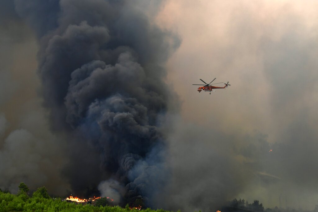 An helicopter operates over a wildfire in Agios Stefanos, in northern Athens, Greece, Friday, Aug. 6, 2021. Thousands of people have fled wildfires burning out of control in Greece and Turkey, including a major blaze just north of the Greek capital of Athens that left one person dead. (AP Photo/Michael Varaklas)