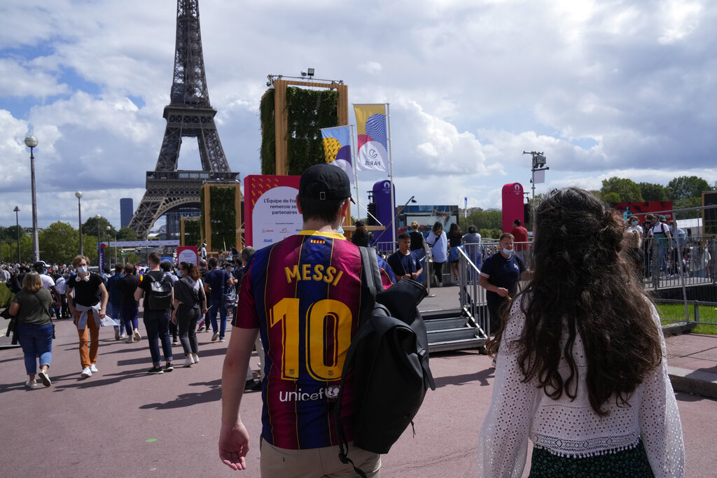 A spectator wears a Lionel Messi soccer jersey as he walks in the Olympics fan zone in the Trocadero Gardens in front of the Eiffel Tower in Paris, Sunday, Aug. 8, 2021. Celebrations were held in Paris Sunday as part of the handover ceremony of Tokyo 2020 to Paris 2024, as Paris will be the next Summer Games host in 2024. The passing of the hosting baton will be split between the Olympic Stadium in Tokyo and a public party and concert in Paris. (AP Photo/Francois Mori)