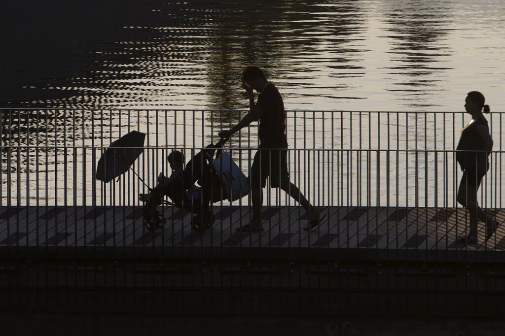 A man pushes a baby buggy with a sun umbrella across a bridge in Madrid, Spain, Thursday, July 9, 2015. Spain has been in a heat wave for nearly two weeks, with temperatures reaching 40 C (104 F).The heatwave is expected to last around another week. (AP Photo/Paul White)