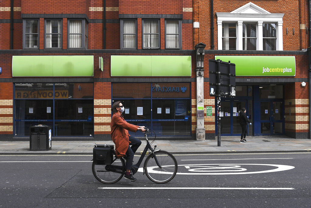 FILE - In this Thursday, April 30, 2020 file photo, a woman wearing a mask to protect against coronavirus, rides a bicycle past a job centre in Shepherd's Bush, as the lockdown to curb the spread of coronavirus continues, in London. The U.K. economy has officially fallen into a recession after official figures showed it contracting by a record 20.4% in the second quarter as a result of lockdown measures put in place to counter the coronavirus pandemic. The slump recorded by the Office for National Statistics follows a 2.2% quarterly contraction in the first three months of the year.  (AP Photo/Alberto Pezzali, File)
