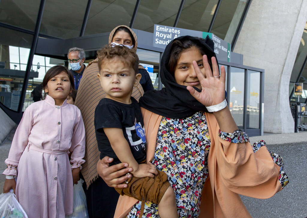 A girl evacuated from Kabul, Afghanistan, waves as she walk to board a bus at Washington Dulles International Airport, in Chantilly, Va., on Saturday, Aug. 28, 2021. (AP Photo/Gemunu Amarasinghe)