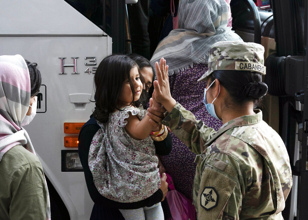 FILE - In this Monday, Aug. 30, 2021, file photo, Army Pfc. Kimberly Hernandez gives a high-five to a girl evacuated from Kabul, Afghanistan, before boarding a bus after they arrived at Washington Dulles International Airport, in Chantilly, Va. U.S. religious groups of many faiths are gearing up to assist the thousands of incoming refugees. (AP Photo/Jose Luis Magana, File)