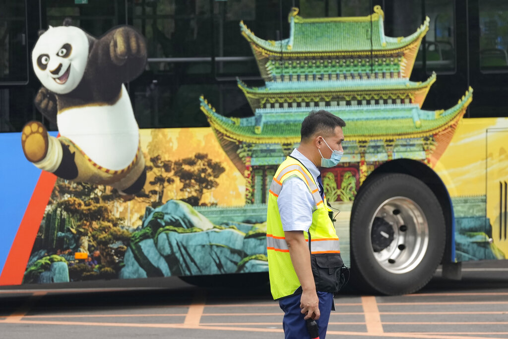 A traffic warden stands near a bus with an advertisement for the Universal Studios theme park during trial runs in Beijing, China, Tuesday, Aug. 31, 2021. Universal Studios announced Monday, Aug. 30, 2021, that its first theme park in China will open in the country's capital in September. The company set the opening date for Sept. 20, according to a statement and video posted on the Chinese social media site WeChat. (AP Photo/Ng Han Guan)