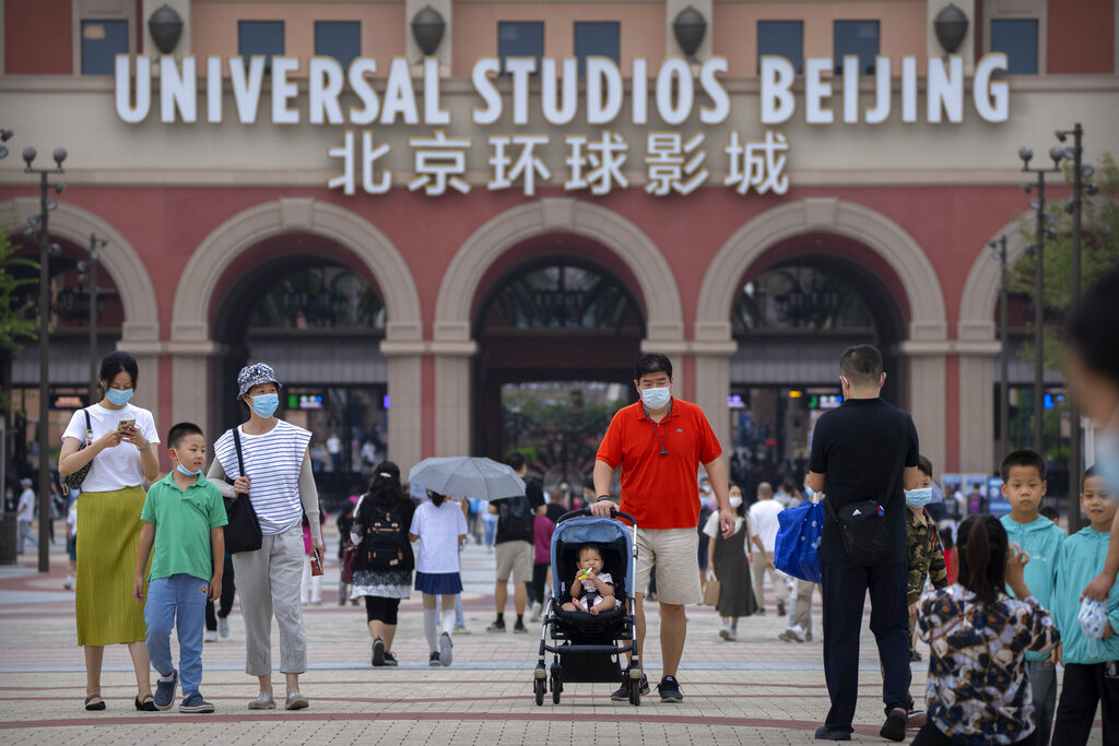 People wearing face masks to help protect against the COVID-19 walk outside the entrance to Universal Studios Beijing in Beijing, Saturday, Sept. 4, 2021. The newest location of the global brand of theme parks officially opens on Sept. 20, though an adjacent shopping and entertainment district opened to the public this week. (AP Photo/Mark Schiefelbein)