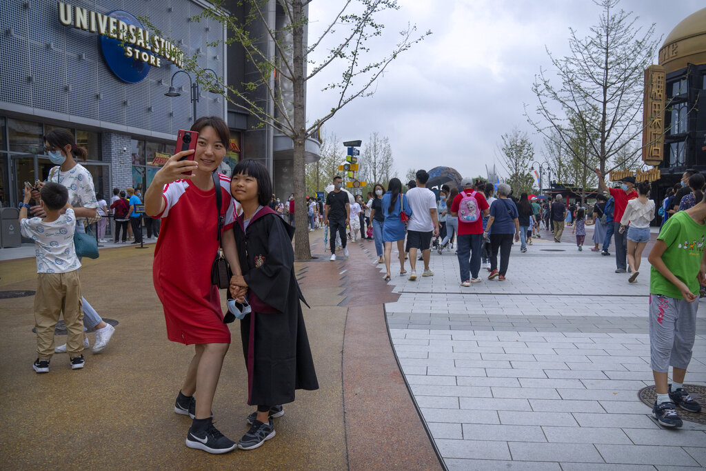 A woman and a girl wearing a wizard costume pose for a selfie in a plaza near the entrance to Universal Studios Beijing in Beijing, Saturday, Sept. 4, 2021. The newest location of the global brand of theme parks officially opens on Sept. 20, though an adjacent shopping and entertainment district opened to the public this week. (AP Photo/Mark Schiefelbein)