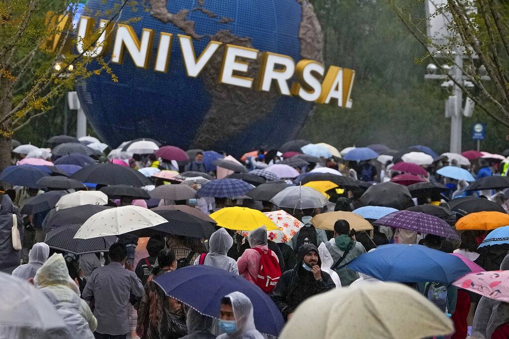 People wearing raincoats and carrying umbrellas walk through a plaza near the entrance of Universal Studios Beijing in Beijing, Monday, Sept. 20, 2021. Thousands of people brave the rain visit to the newest location of the global brand of theme parks which officially opens on Monday. (AP Photo/Andy Wong)