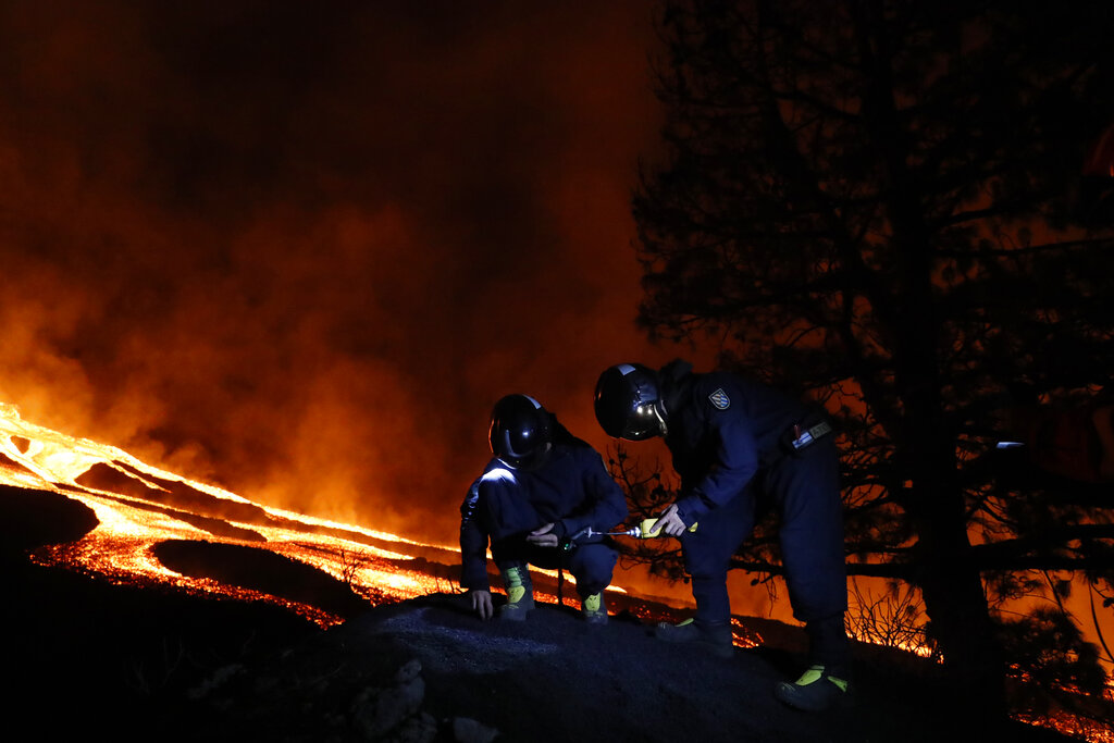 Military Emergency Unit personal take gas reading measurements near a volcano on the Canary island of La Palma, Spain, in the early hours of Tuesday Sept. 28, 2021. Lava flowing from an erupting volcano on the Spanish island of La Palma has picked up pace on its way to the sea. Officials say it is now within about 800 meters (875 yards) of the shoreline. When the molten rock eventually meets the sea water it could trigger explosions and toxic gas. (Luismi Ortiz/UME, via AP)
