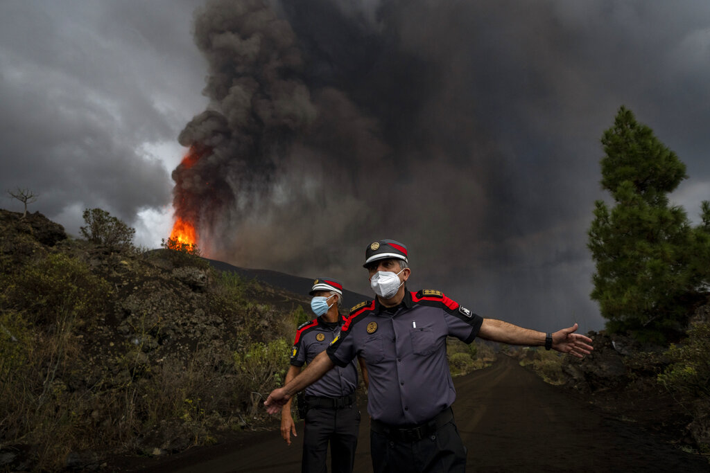A police officer orders journalists to leave the area during a media tour near the volcano on the island of La Palma in the Canaries, Spain, Wednesday, Sept. 22, 2021. A volcano on a small Spanish island in the Atlantic Ocean erupted on Sunday, forcing the evacuation of thousands of people. Experts say the volcanic eruption and its aftermath on a Spanish island could last for up to 84 days. The Canary Island Volcanology Institute said Wednesday it based its calculation on the length of previous eruptions on the archipelago. (AP Photo/Emilio Morenatti)